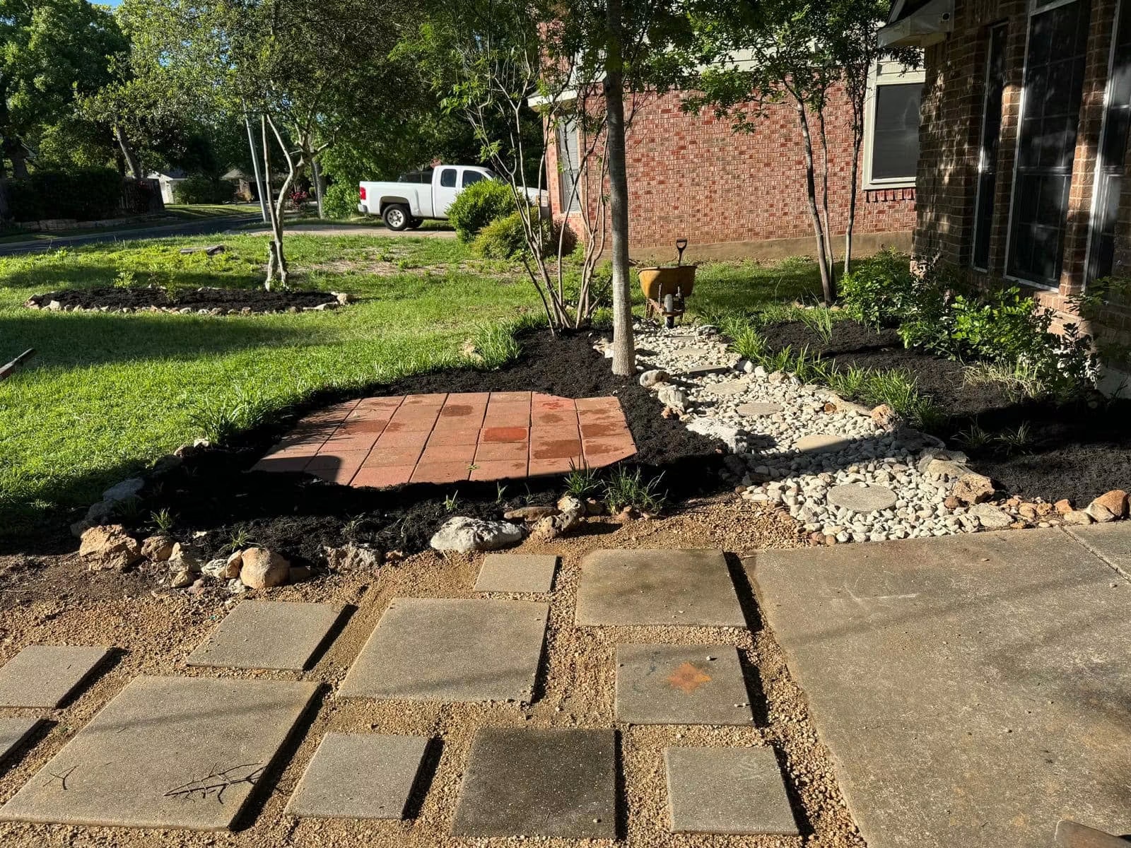 Front-yard installation in progress with a paver landing, stepping stones, river rock, and mulched beds