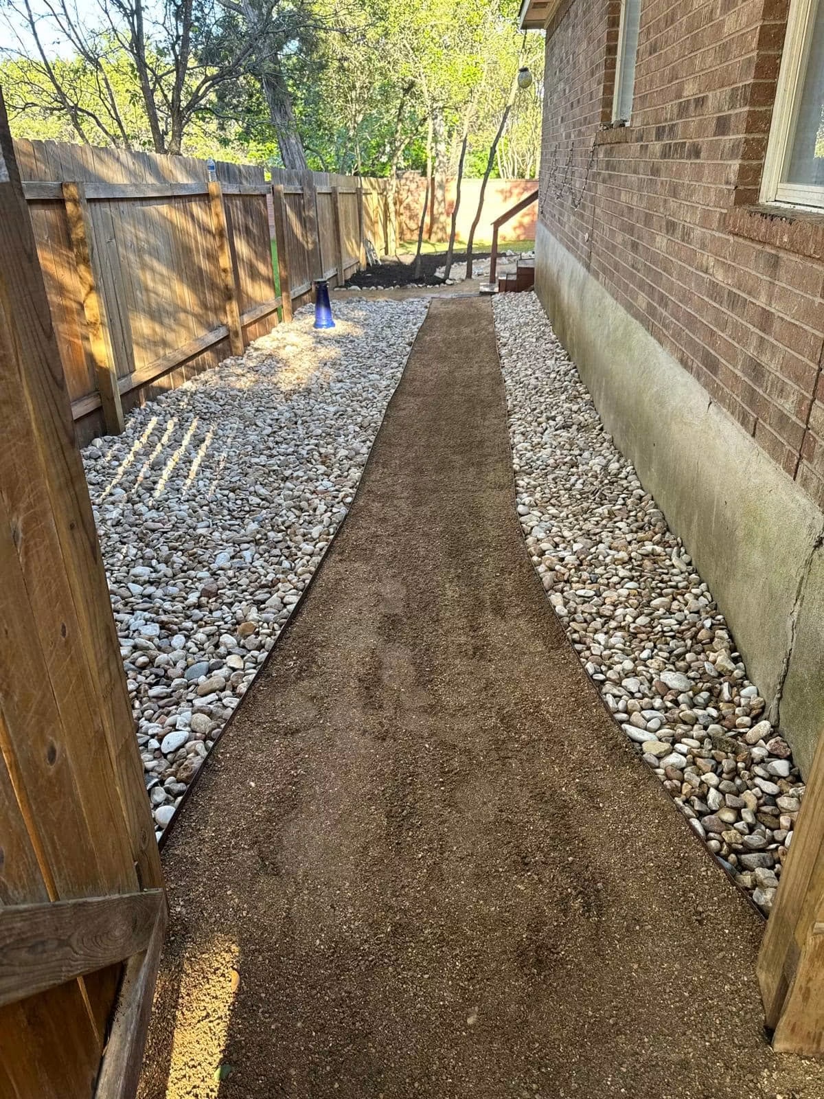 Completed compacted residential side-yard path bordered with river rock